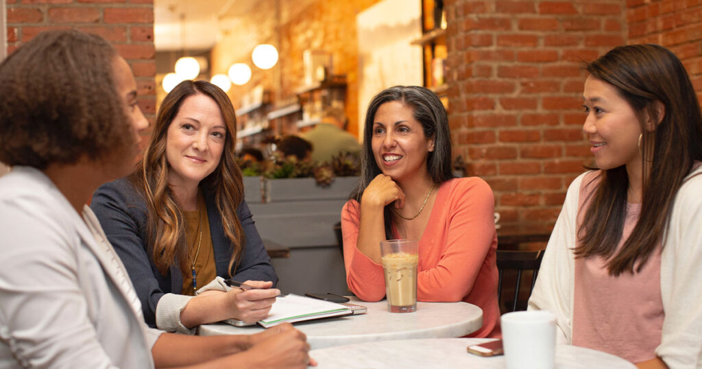 A group of four women are drinking coffee and having a very engaged conversation